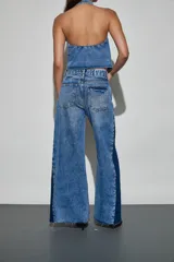 Jean de denim en tonos azul claro y azul oscuro, de tiro alto y corte wide leg, con inserciones laterales en contraste, detalles de tachas metálicas y acabado desmechado en el ruedo.