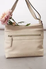 Cartera de cuero color beige, de diseño estructurado, con bolsillo frontal con cierre y detalles en cuero grabado con efecto reptil. Cuenta con correa ajustable para llevar al hombro o cruzada.