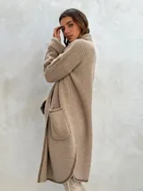 Sacón de punto color crudo con ribetes marrones, de corte largo y holgado, con cuello redondo, mangas largas y dos bolsillos frontales.