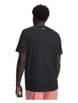 Remera de manga corta Under Armour con cuello redondo acanalado. Presenta un diseño gráfico frontal con el logo de la marca, tipografía retro y patrón de tablero de ajedrez en tonos rosado, celeste y blanco sobre fondo negro.