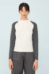 Sweater de punto bicolor, con cuerpo blanco con diseño de trenzas y mangas ranglan grises.