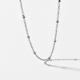 Cadena plateada de acero con eslabones y pequeñas cuentas redondas distribuidas a lo largo de la cadena.