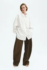 Camisa oversized blanca con finas rayas verticales beige, de manga larga y cierre frontal con botones.