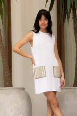 Vestido corto tejido en hilado de algodón en punto dolor, color blanco, con cuello redondo y sin mangas. Presenta dos bolsillos de lino aplicados en el frente.