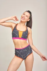 Top deportivo de estilo bikini con diseño estampado multicolor en tonos neón, con detalles en negro en el centro y en la banda inferior. Cuenta con breteles anchos y fijos, y copas removibles.