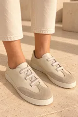 Championes de cuero vacuno color beige, con puntera combinada en gamuza, suela de goma y cordones elásticos planos a rayas.