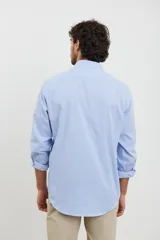 Camisa celeste con rayas verticales blancas, de manga larga con puños abotonados y cuello clásico.