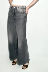 Jeans de tiro medio con diseño wide leg y cinco bolsillos. Presenta costuras verticales marcadas en el delantero y cierre frontal con cremallera y botón.