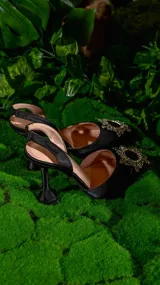 Zapato de vestir negro de satén con punta fina y detalle de aplique brillante en forma de sol.