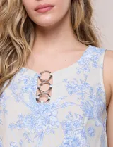 Blusa de lino y rayón color beige con estampado floral en tonos celestes, sin mangas, con escote redondo y detalle de tres aros metálicos plateados entrelazados en el frente.