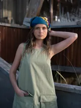 Vestido corto verde oliva, sin mangas, con cuello redondo y dos bolsillos grandes tipo parche en el frente.