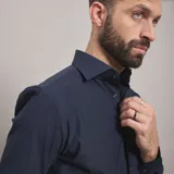 Camisa de vestir negra de manga larga, confeccionada en tejido técnico elástico y libre de arrugas, con cuello clásico y cierre frontal de botones.