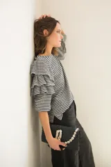 Blusa de tela con estampado vichy en blanco y negro, con cuello redondo y mangas con tres volados escalonados que llegan hasta el codo. Presenta puños elásticos y cierre con botón en la parte posterior.