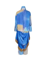 Conjunto de tres piezas inspirado en la vestimenta tradicional uruguaya, compuesto por camisa, pantalón tipo chiripá y accesorio, confeccionado en tela satinada con estampado artístico sublimado en tonos azules y amarillos, con terminaciones de flecos en color marrón.