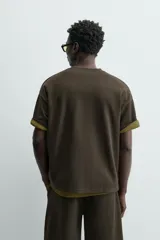 Sudadera de manga corta con cuello redondo, confeccionada en tejido texturizado de color verde oscuro/marrón. Presenta un corte relajado (relaxed fit).