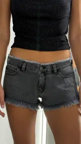 Short de jean tiro bajo color gris oscuro, con diseño de bordes deshilachados en la cintura y en las piernas. Cuenta con cierre frontal, botón metálico y bolsillos laterales.