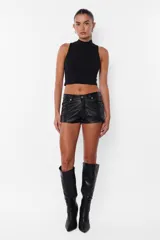 Short negro de cuerina, tiro medio, con bolsillos delanteros y traseros, presillas en la cintura y cierre con botón metálico y cremallera.