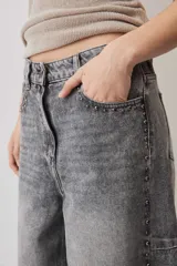 Jeans de corte barrel en tono gris deslavado, con diseño amplio y tachas decorativas a lo largo de las costuras laterales y los bolsillos delanteros.