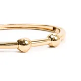 Pulsera rígida dorada con tres esferas decorativas.