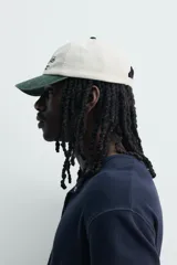 Gorra de seis paneles con efecto lavado, de color blanco crudo con visera en verde militar. Presenta un bordado frontal contrastante con texto en negro y una estrella roja.