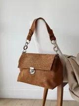 Cartera de cuero marrón con textura croco, cierre frontal metálico y detalles de herrajes plateados.