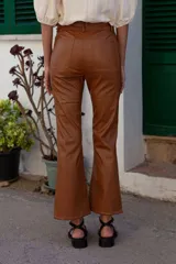 Pantalón de cuero sintético color marrón claro y marrón oscuro, de tiro medio/alto y silueta levemente acampanada desde la rodilla. Tiene bolsillos cuadrados y combina dos colores en frente y espalda.