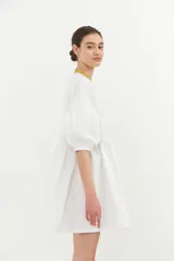 Vestido corto blanco de algodón con lurex, corte evasé, mangas cortas abullonadas y cuello redondo con ribete amarillo.