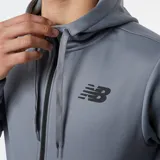 Campera gris de New Balance, modelo Tenacity Performance Fleece, con cierre frontal, capucha con cordones ajustables, bolsillos laterales y logo de la marca en el pecho. Confeccionada con tecnología NB HEAT que ayuda a mantener el calor y elimina la humedad.