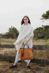 Bolso tipo tote de cuero gamuzado en color marrón, con textura grabada tipo cocodrilo, manijas de cuero oscuro y detalle de borla colgante.