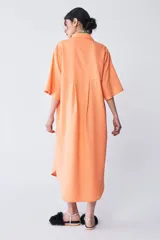 Vestido camisero color naranja de corte amplio, con largo irregular, cuello camisero, escote en V y tajo en los laterales.