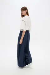Pantalón de jean azul oscuro, tiro alto, corte ancho y holgado, con bolsillos y frunces en la cintura.