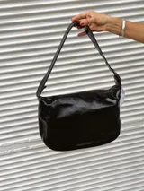 Bolso de hombro con diseño animal print de leopardo, confeccionado en cuero. Presenta una correa ajustable con hebilla metálica y detalles de ojales decorativos en los laterales.