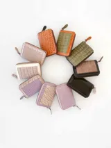 Billetera pequeña con cierre metálico, cuerpo principal de cuero lila texturizado y ribetes en color crema. Presenta un parche de cuero marrón con la palabra "chowie" escrita en cursiva.