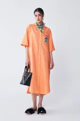 Vestido camisero color naranja de corte amplio, con largo irregular, cuello camisero, escote en V y tajo en los laterales.