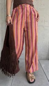 Pantalón de lino a rayas verticales en tonos rojo, naranja, marrón y rosa, con cierre y botón, y dos bolsillos laterales.