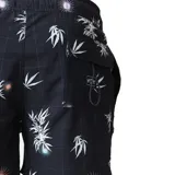 Short de baño negro con estampado de hojas de palma blancas y detalles de destellos de luz en naranja y celeste.