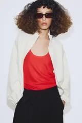 Chaqueta de punto color crudo con cuello alto, cierre frontal de cremallera metálica, mangas largas con puños elásticos y bajo ajustable con cordones.