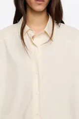 Camisa oversize de algodón color celeste, con cuello camisero, botones frontales y mangas largas ranglán con puños abotonados. Presenta pespuntes a contraste en toda la prenda.