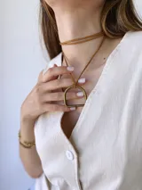 Colgante con cordón de cuero color camel y dije metálico dorado con forma de estribo.