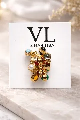 Anillo con base metálica de acabado dorado, con diseño envolvente adornado con múltiples dijes colgantes que incluyen piedras de colores (azul claro, negro, rojo, amarillo, verde) y una perla blanca.