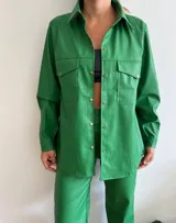 Camisa verde con textura de cocodrilo, de mangas largas y corte holgado. Presenta dos bolsillos con solapa en el pecho y cierre frontal con botones.