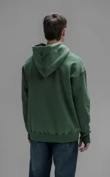 Hoodie oversize color verde, confeccionado en frisa premium con textura gamuzada. Presenta capucha ajustable con cordones personalizados, bolsillo frontal tipo canguro y puños con abertura para pulgar.