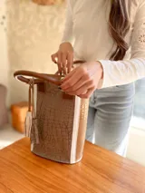 Bolso matero de cuero color taupe con textura croco y detalles en cuero color marrón. Tiene doble asa de mano y un dije de borla.