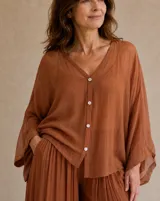 Camisa oversize color terracota, con escote en V, cierre frontal con botones claros y mangas anchas y fluidas de corte largo.