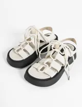 Sandalias blancas de cuero vegano con tiras anchas y cordones para atar al tobillo. Suela de goma negra.