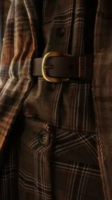 Blazer de largo medio con diseño a cuadros en tonos tierra, confeccionado en mezcla de algodón y poliéster. Presenta solapas clásicas, bolsillos laterales y un cinto de cuero fino incorporado para ajustar la cintura.