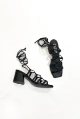 Sandalias negras de cuero sintético con tiras finas que se atan al tobillo.