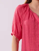 Blusa color fucsia con estampado de rayas verticales y flores, cuello redondo con escote en V y mangas cortas abullonadas.