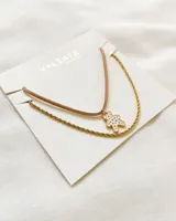 Collar doble con cadena dorada y tiento marrón, con dije de oso blanco con contorno dorado.