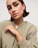 Pulsera de bolitas de metal bañado en plata con dije de candado grabado con el logo de la marca.